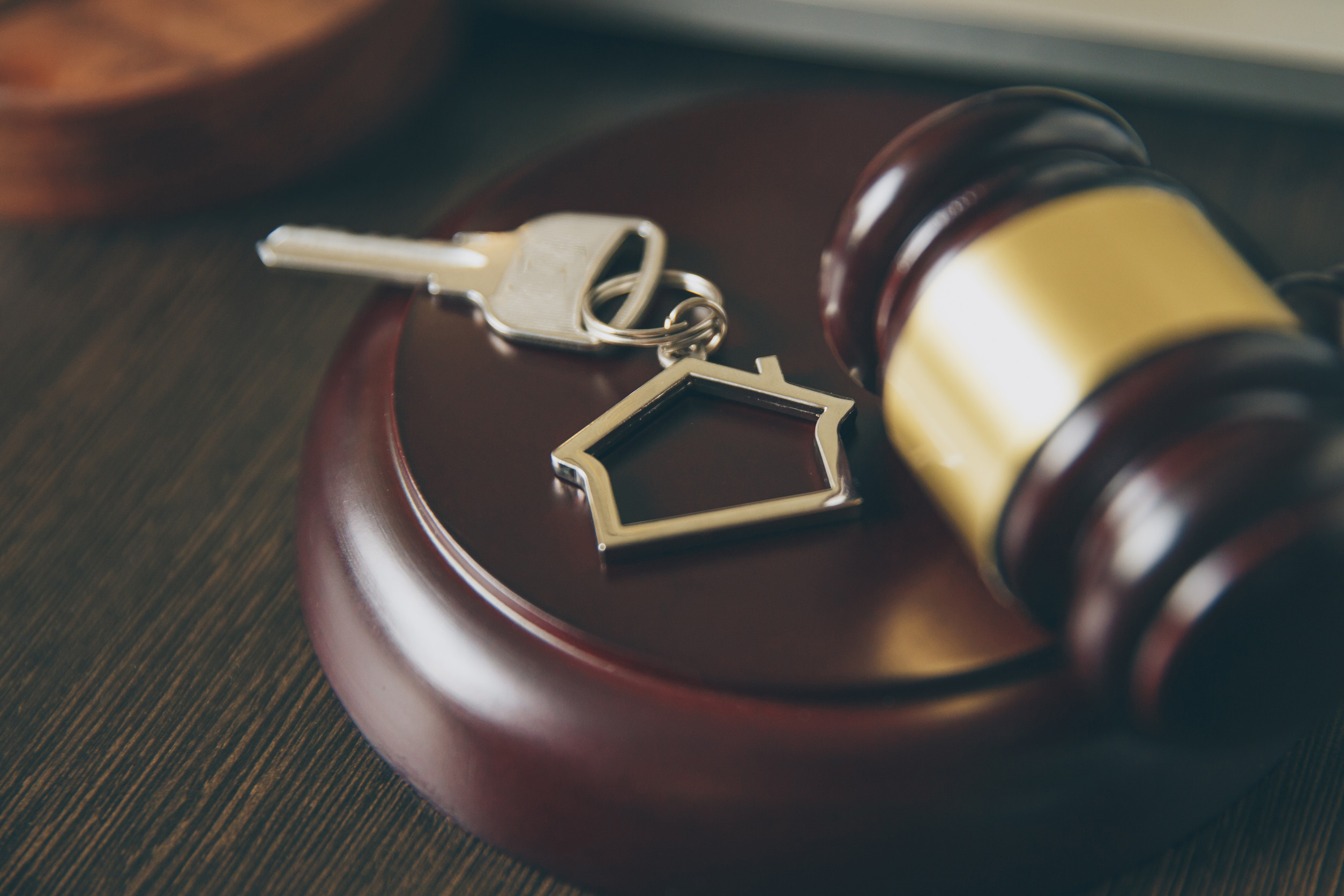 A gavel rests on a wooden table next to a house-shaped keychain with a key, symbolizing property rights or real estate law involving property owners and easements.