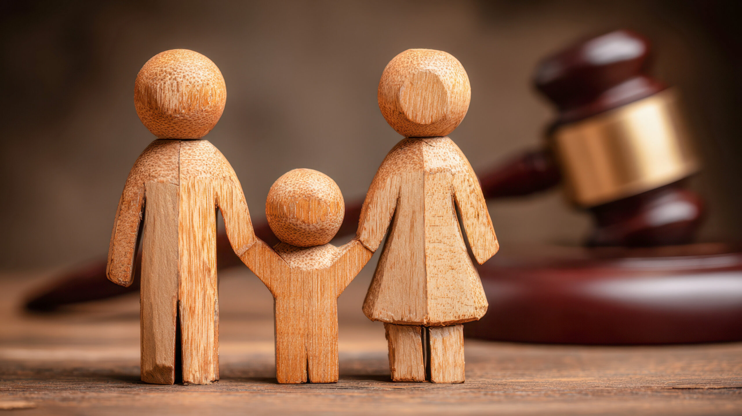 Three wooden figures representing a family stand together in front of a judge's gavel, symbolizing family law cases or legal proceedings involving families.