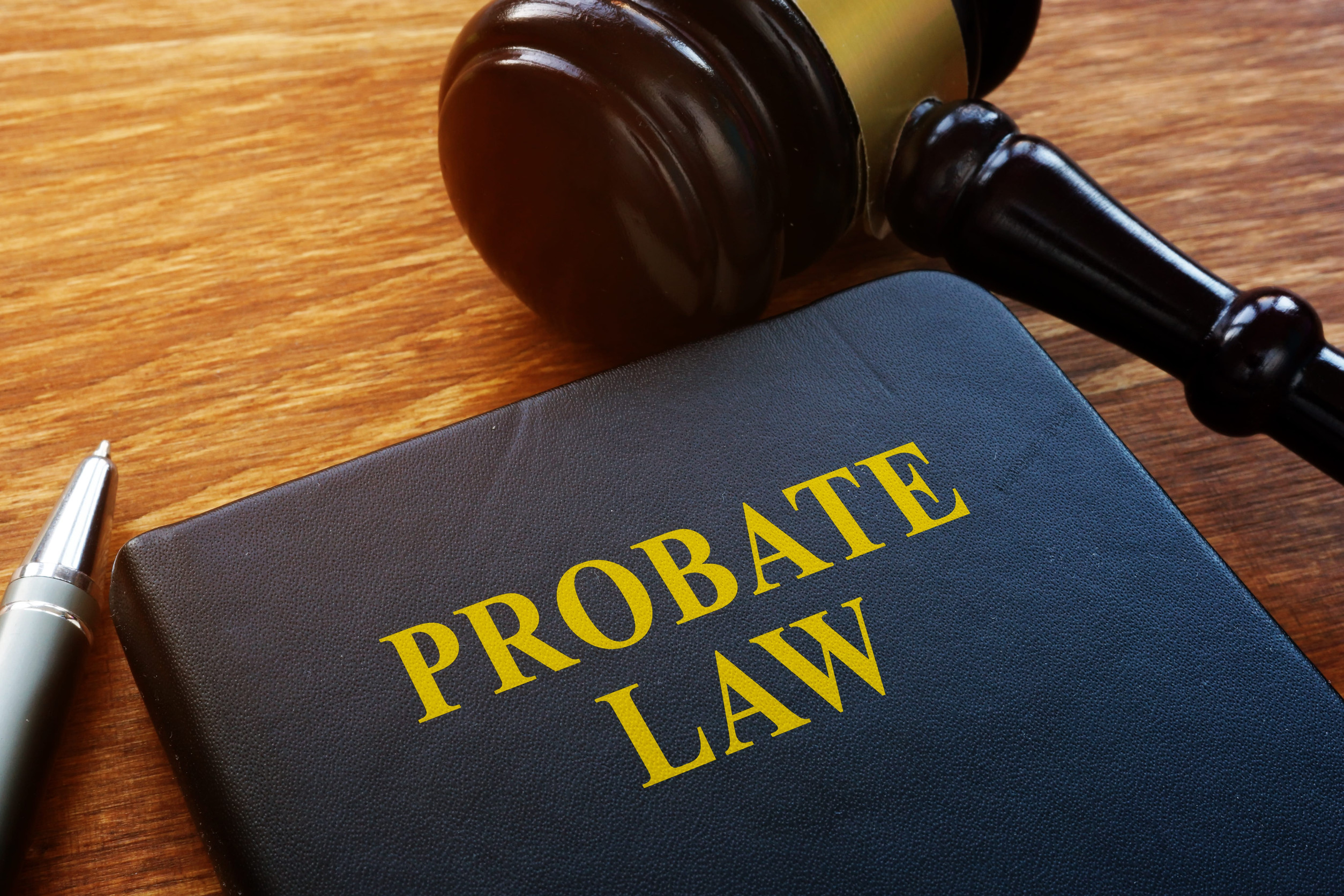 A black book titled "PROBATE LAW" in yellow letters lies on a wooden table next to a silver pen and a judge’s gavel, illustrating the probate process in Minnesota.