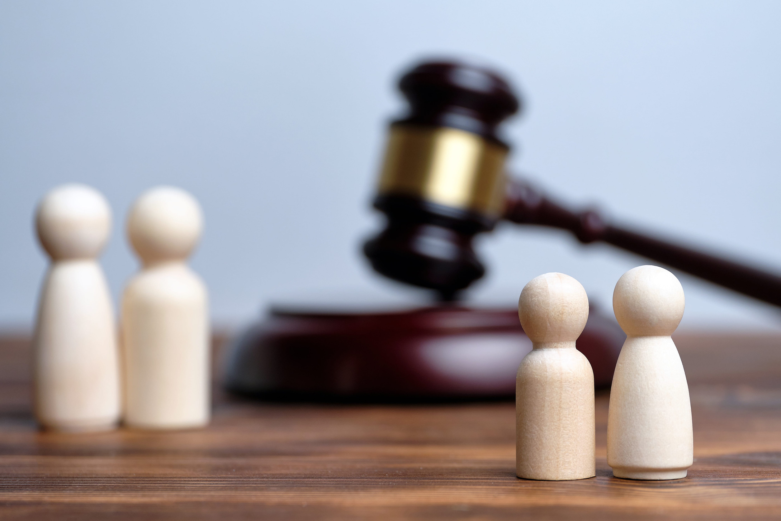 Two pairs of wooden figurines face each other with a judge's gavel in the background, symbolizing a legal dispute—possibly about family matters or separation, such as child custody under Minnesota child custody laws.