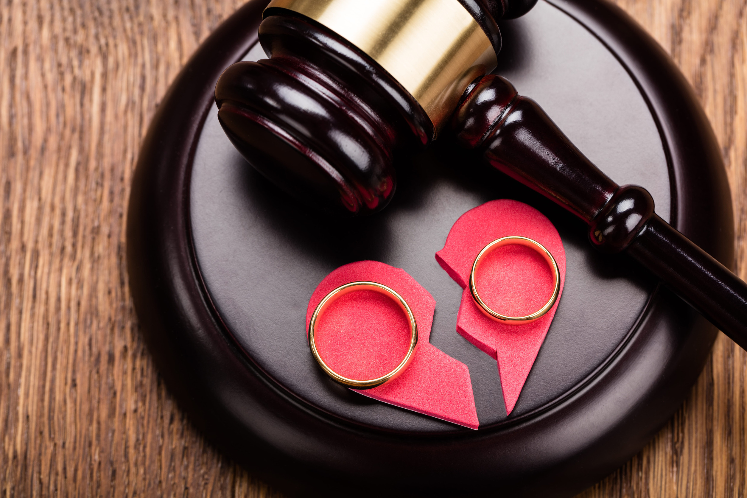 A judge’s gavel rests on a block next to two gold wedding rings placed on a broken red paper heart, symbolizing divorce or separation and raising questions about the Minnesota divorce timeline.