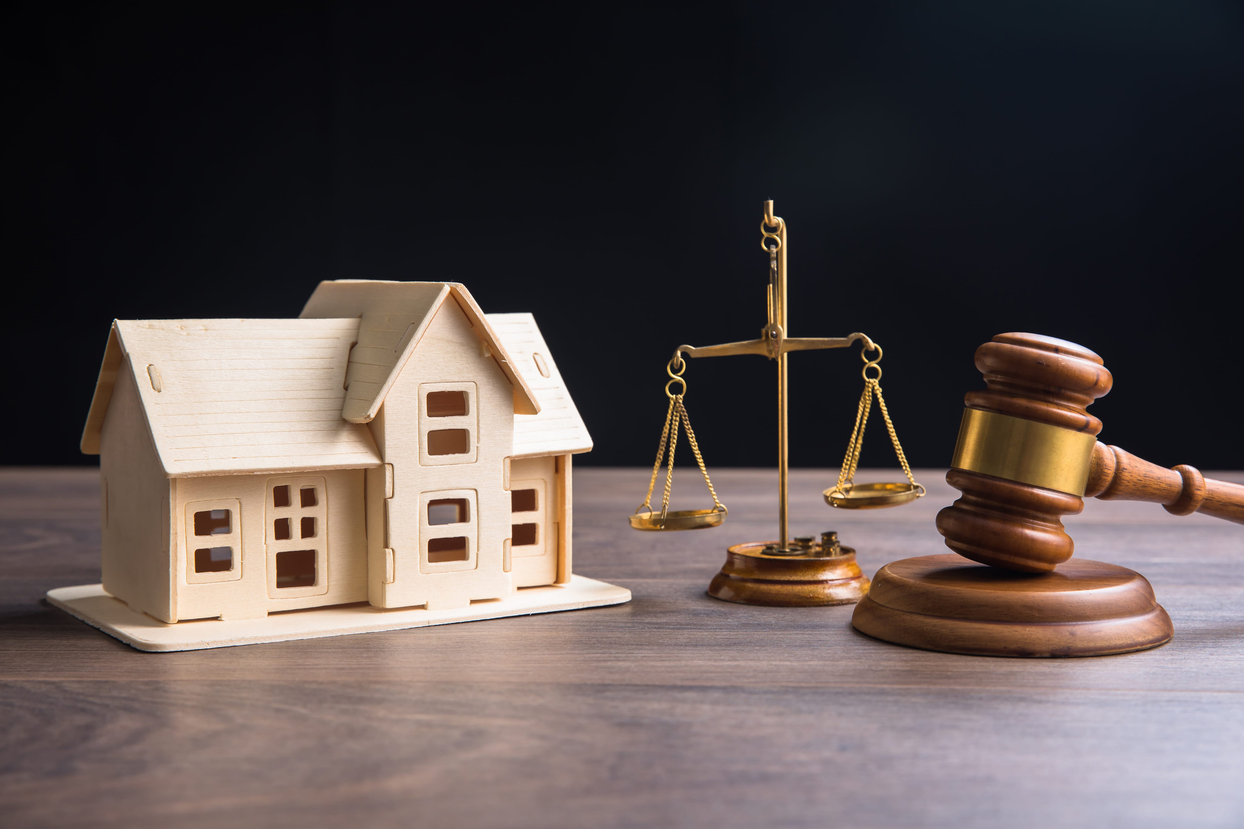 A wooden model house, a brass balance scale, and a judge's gavel rest on a wooden table against a dark background, symbolizing an overview of Minnesota real estate law and probate legal proceedings.