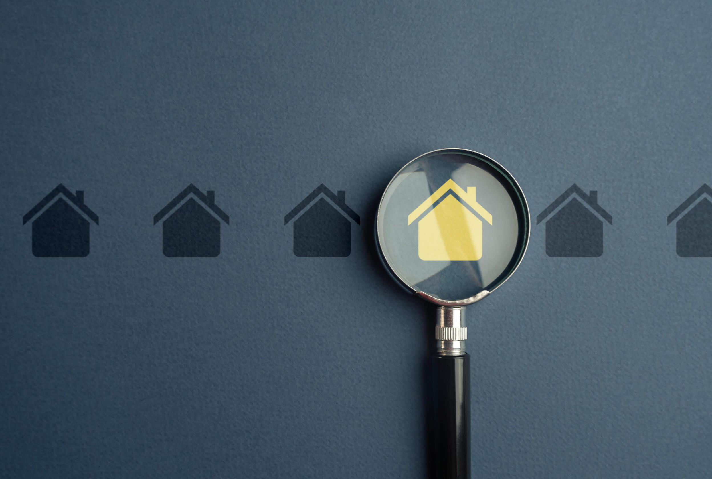 A magnifying glass focuses on a yellow house icon among a row of dark house icons on a blue background, symbolizing searching for a home or Minnesota Real Estate, with an emphasis on title searches and the real estate selection process.