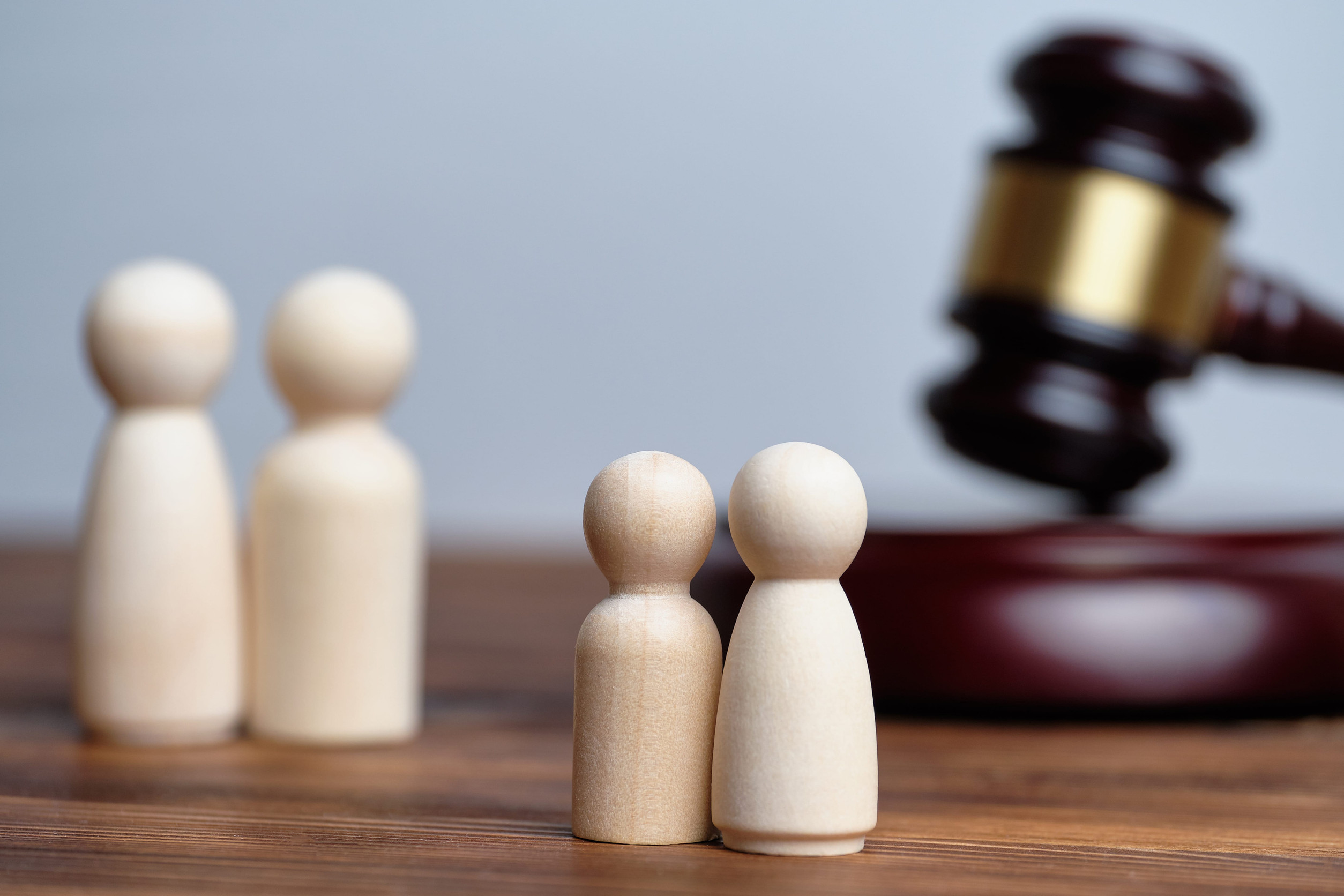 Two pairs of wooden figures stand on a table with a judge’s gavel in the background, suggesting a legal or family court context—perhaps illustrating how child custody is determined in Minnesota.