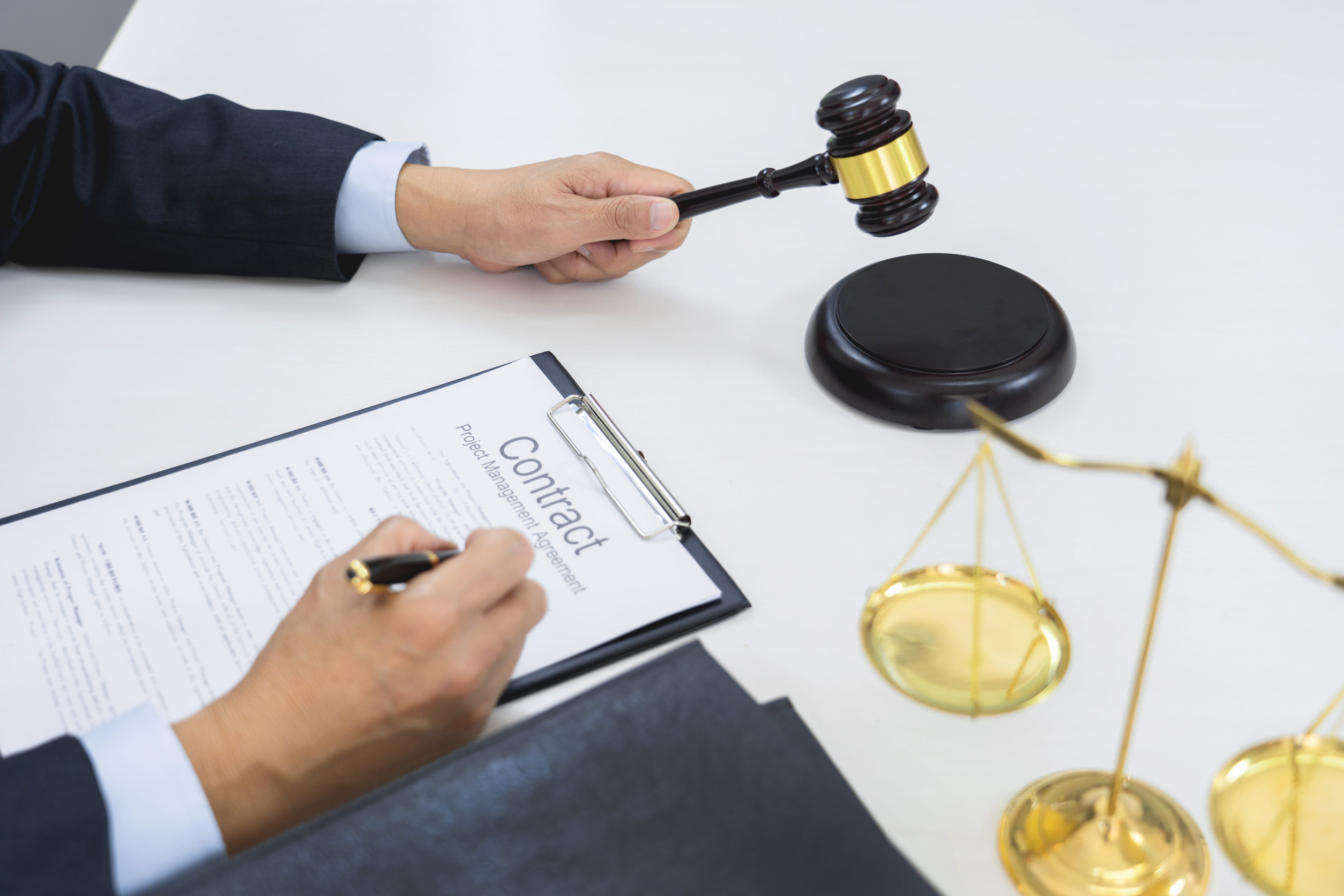 A Minnesota attorney in a suit signs a project management agreement, with a gavel and a scale of justice resting on the table.