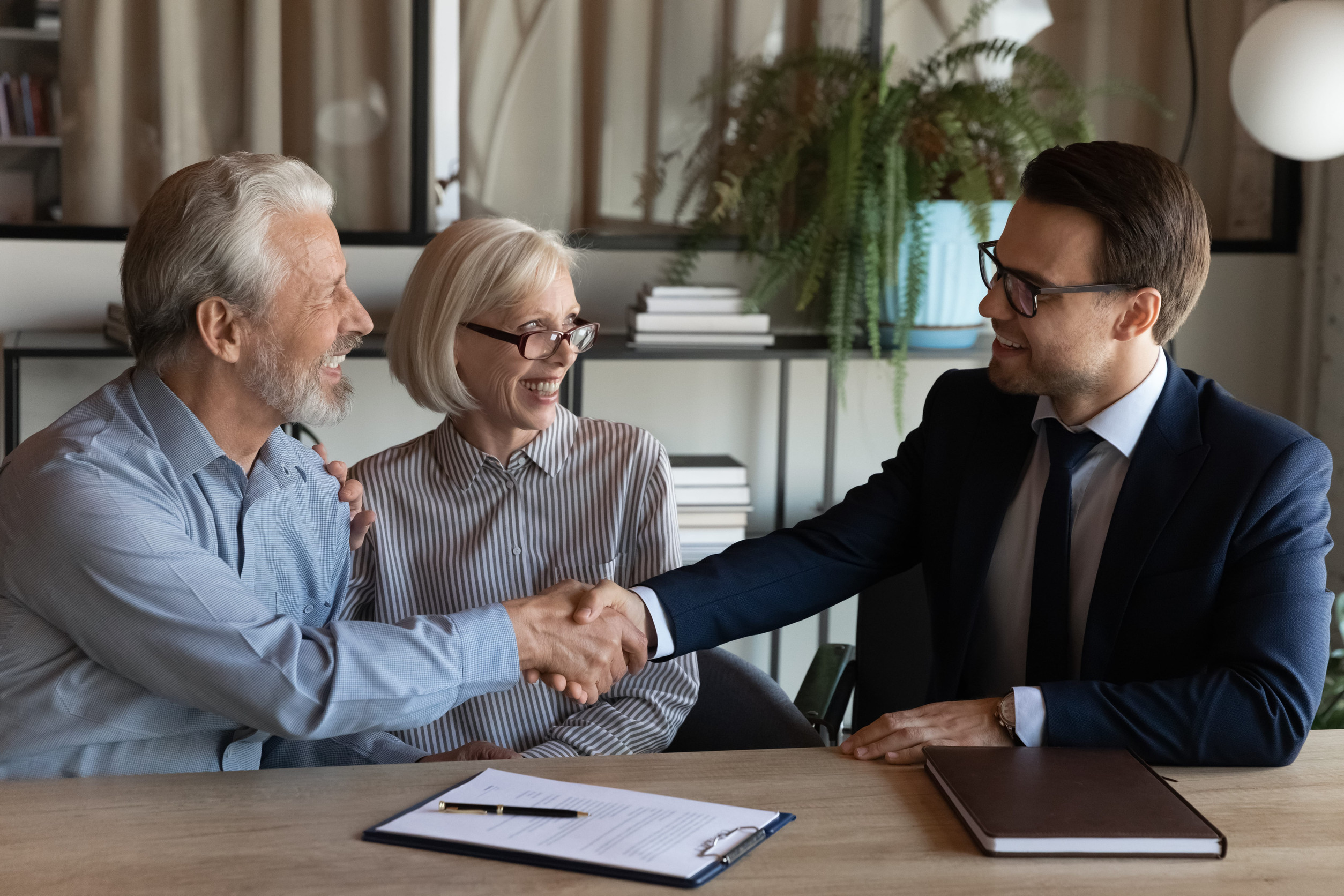 An older couple shaking hands with a professional man in a suit across a desk during an estate planning consultation.