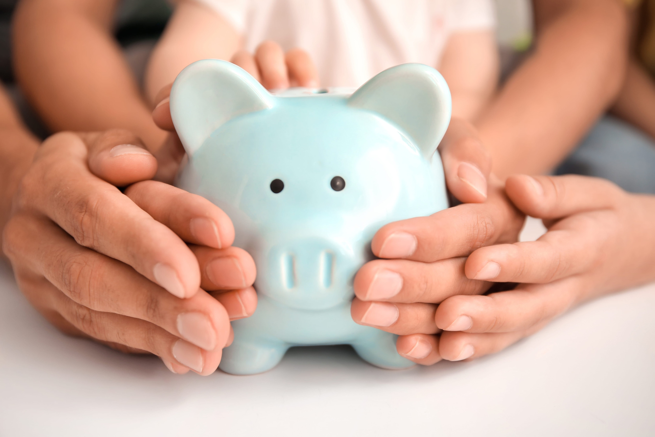 Adult and child hands holding a light blue piggy bank while considering how to calculate child support.
